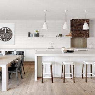 Photo of a large contemporary galley eat-in kitchen in Melbourne with an undermount sink, glass-front cabinets, white cabinets, white splashback, timber splashback, light hardwood floors, with island and beige floor.