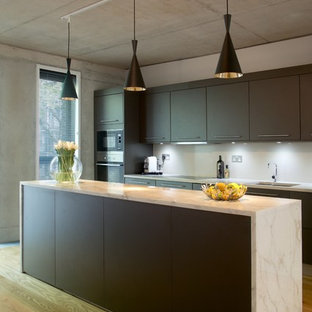 Immagine di una cucina parallela industriale con lavello sottopiano, ante lisce, ante marroni, paraspruzzi bianco, elettrodomestici in acciaio inossidabile, pavimento in legno massello medio e isola