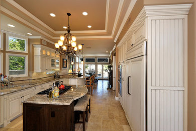 Example of a mid-sized transitional u-shaped travertine floor and brown floor eat-in kitchen design in Orange County with a double-bowl sink, raised-panel cabinets, white cabinets, granite countertops, beige backsplash, stainless steel appliances, an island and subway tile backsplash