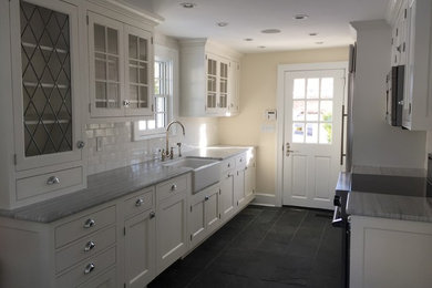 Open concept kitchen - mid-sized transitional galley slate floor and gray floor open concept kitchen idea in New York with a farmhouse sink, shaker cabinets, white cabinets, quartzite countertops, white backsplash, subway tile backsplash, stainless steel appliances and no island