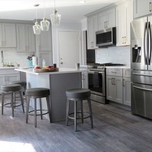 This is an example of a contemporary l-shaped eat-in kitchen in New York with a drop-in sink, flat-panel cabinets, grey cabinets, limestone benchtops, white splashback, stone tile splashback, coloured appliances, laminate floors, with island, grey floor and white benchtop.