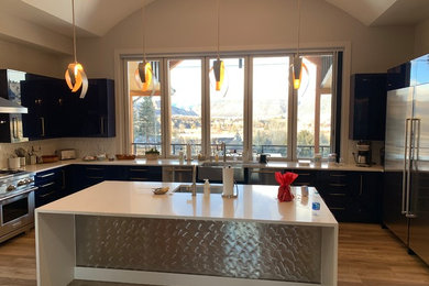 This is an example of a medium sized modern u-shaped kitchen/diner in Denver with a belfast sink, flat-panel cabinets, black cabinets, engineered stone countertops, white splashback, ceramic splashback, stainless steel appliances, light hardwood flooring, an island, brown floors and white worktops.