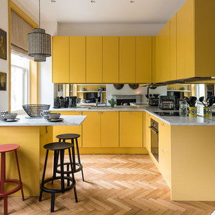Kleine Nordische Küche in L-Form mit Unterbauwaschbecken, flächenbündigen Schrankfronten, gelben Schränken, Rückwand aus Spiegelfliesen, braunem Holzboden und Halbinsel in London