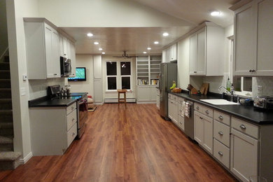 Example of a mid-sized classic galley vinyl floor and brown floor open concept kitchen design in Salt Lake City with white cabinets, white backsplash, stainless steel appliances, a single-bowl sink, ceramic backsplash, shaker cabinets, solid surface countertops and no island