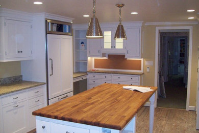 Example of a large l-shaped medium tone wood floor kitchen design in Philadelphia with white cabinets, granite countertops, stainless steel appliances and an island