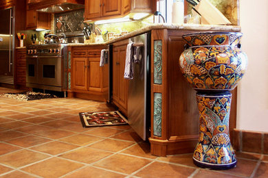 Example of a large tuscan l-shaped terra-cotta tile eat-in kitchen design in Orange County with an undermount sink, raised-panel cabinets, medium tone wood cabinets, granite countertops, beige backsplash, stone tile backsplash, stainless steel appliances and an island