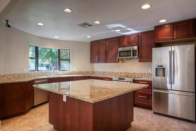Example of a large l-shaped enclosed kitchen design in Las Vegas with an undermount sink, recessed-panel cabinets, dark wood cabinets, granite countertops, metallic backsplash, mosaic tile backsplash, stainless steel appliances and an island
