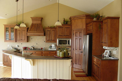 クリーブランドにある中くらいな地中海スタイルのおしゃれなキッチン (落し込みパネル扉のキャビネット、中間色木目調キャビネット、ベージュキッチンパネル、シルバーの調理設備、淡色無垢フローリング) の写真