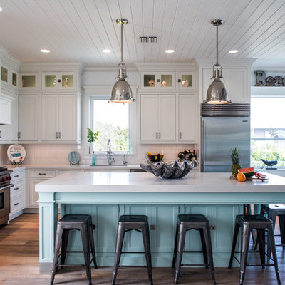 Inspiration for a mid-sized coastal l-shaped medium tone wood floor and brown floor open concept kitchen remodel in Other with shaker cabinets, white cabinets, white backsplash, subway tile backsplash, stainless steel appliances, an island, an undermount sink and solid surface countertops