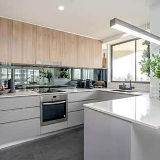 Inspiration for a mid-sized contemporary u-shaped kitchen in Gold Coast - Tweed with an undermount sink, flat-panel cabinets, white splashback, glass sheet splashback, porcelain floors, a peninsula, grey floor and white benchtop.