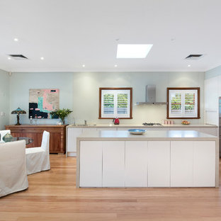 Inspiration for a transitional l-shaped eat-in kitchen in Sydney with an undermount sink, flat-panel cabinets, white cabinets, solid surface benchtops, green splashback, glass sheet splashback, stainless steel appliances, light hardwood floors, with island and beige benchtop.