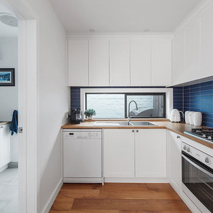 Contemporary l-shaped kitchen in Melbourne with a drop-in sink, shaker cabinets, white cabinets, wood benchtops, blue splashback, white appliances, medium hardwood floors, brown floor and brown benchtop.