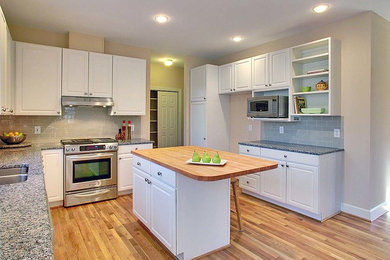 Mid-sized transitional u-shaped medium tone wood floor and brown floor enclosed kitchen photo in Raleigh with a double-bowl sink, raised-panel cabinets, white cabinets, granite countertops, blue backsplash, subway tile backsplash, stainless steel appliances and an island