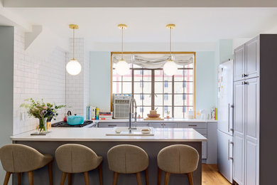 Photo of a traditional u-shaped kitchen in New York with a built-in sink, grey cabinets, white splashback, metro tiled splashback, medium hardwood flooring and a breakfast bar.