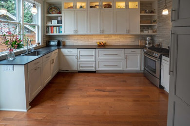 Example of a mid-sized classic u-shaped medium tone wood floor and brown floor enclosed kitchen design in Portland with an undermount sink, shaker cabinets, white cabinets, solid surface countertops, gray backsplash, ceramic backsplash, stainless steel appliances, no island and black countertops