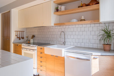 モントリオールにあるお手頃価格の中くらいなコンテンポラリースタイルのおしゃれなキッチン (シングルシンク、フラットパネル扉のキャビネット、中間色木目調キャビネット、タイルカウンター、白いキッチンパネル、セラミックタイルのキッチンパネル、白い調理設備、セラミックタイルの床、グレーの床) の写真