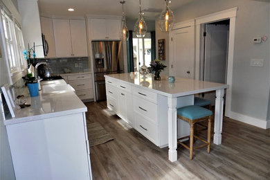 Design ideas for a traditional l-shaped kitchen/diner in San Diego with a belfast sink, shaker cabinets, white cabinets, engineered stone countertops, blue splashback, glass tiled splashback, stainless steel appliances, light hardwood flooring, an island and grey floors.