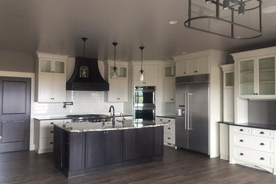 Large elegant l-shaped dark wood floor and brown floor eat-in kitchen photo in Boise with a farmhouse sink, shaker cabinets, white cabinets, soapstone countertops, white backsplash, subway tile backsplash, stainless steel appliances, an island and black countertops
