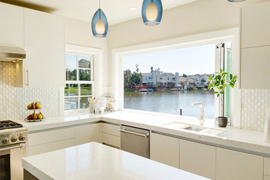 Bild på ett funkis kök, med en undermonterad diskho, släta luckor, vita skåp, marmorbänkskiva, vitt stänkskydd, stänkskydd i glaskakel, rostfria vitvaror, ljust trägolv och en köksö