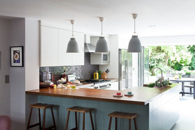 Inspiration for a contemporary kitchen in London with flat-panel cabinets, white cabinets, black splashback, metro tiled splashback and stainless steel appliances.