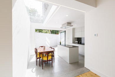 Photo of a small contemporary l-shaped open plan kitchen in London with a submerged sink, flat-panel cabinets, grey cabinets, glass sheet splashback, black appliances, concrete flooring, an island, grey floors and black worktops.