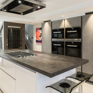 This is an example of a medium sized contemporary kitchen in London with flat-panel cabinets, stainless steel appliances, an island, beige floors, black worktops and grey cabinets.