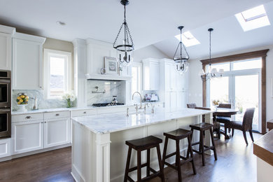 Eat-in kitchen - large transitional l-shaped medium tone wood floor and brown floor eat-in kitchen idea in Seattle with a farmhouse sink, shaker cabinets, white cabinets, granite countertops, white backsplash, marble backsplash, stainless steel appliances, an island and white countertops