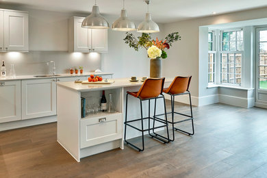 Foto de cocina tradicional renovada de tamaño medio con fregadero integrado, armarios con puertas mallorquinas, salpicadero blanco, electrodomésticos blancos, suelo de madera pintada, península y suelo marrón