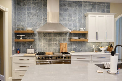 クリーブランドにある広いコンテンポラリースタイルのおしゃれなキッチン (アンダーカウンターシンク、シェーカースタイル扉のキャビネット、白いキャビネット、珪岩カウンター、青いキッチンパネル、セラミックタイルのキッチンパネル、シルバーの調理設備、淡色無垢フローリング、茶色い床、白いキッチンカウンター) の写真