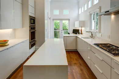 Inredning av ett modernt litet kök, med en enkel diskho, luckor med glaspanel, vita skåp, bänkskiva i kvarts, vitt stänkskydd, rostfria vitvaror, mellanmörkt trägolv och en köksö
