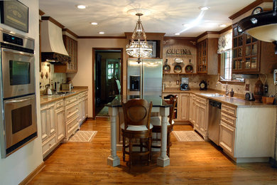 Mid-sized tuscan u-shaped medium tone wood floor and brown floor eat-in kitchen photo in Indianapolis with an undermount sink, raised-panel cabinets, beige cabinets, stainless steel appliances, an island, granite countertops, beige backsplash and stone tile backsplash