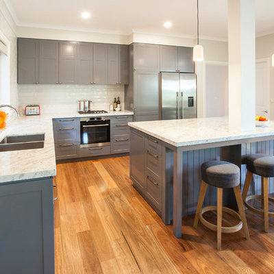 Open concept kitchen - mid-sized traditional l-shaped medium tone wood floor open concept kitchen idea in Melbourne with an undermount sink, shaker cabinets, gray cabinets, granite countertops, beige backsplash, subway tile backsplash, stainless steel appliances, an island and white countertops