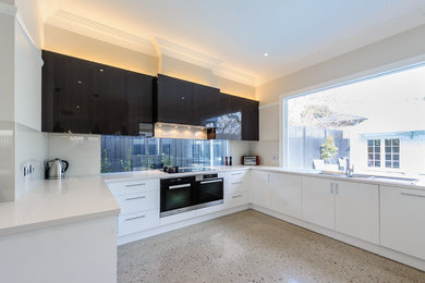 Modern inredning av ett kök och matrum, med släta luckor, vita skåp, glaspanel som stänkskydd, rostfria vitvaror, en undermonterad diskho, bänkskiva i kvartsit och betonggolv