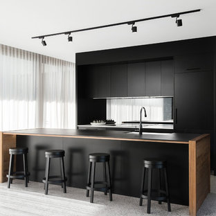 This is an example of a mid-sized contemporary galley eat-in kitchen in Hobart with an undermount sink, flat-panel cabinets, black cabinets, mirror splashback, with island, black benchtop, laminate benchtops, black appliances and terrazzo floors.