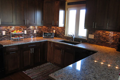 Example of a large classic u-shaped medium tone wood floor open concept kitchen design in Milwaukee with an undermount sink, shaker cabinets, dark wood cabinets, granite countertops, multicolored backsplash and black appliances
