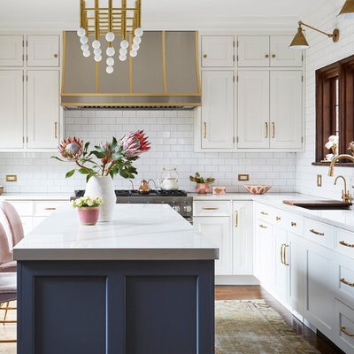 Example of a transitional l-shaped dark wood floor and brown floor kitchen design in Chicago with an undermount sink, shaker cabinets, white cabinets, white backsplash, subway tile backsplash, stainless steel appliances, an island and white countertops