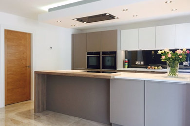 This is an example of a medium sized contemporary open plan kitchen in Other with flat-panel cabinets, white cabinets, mirror splashback, black appliances and a breakfast bar.