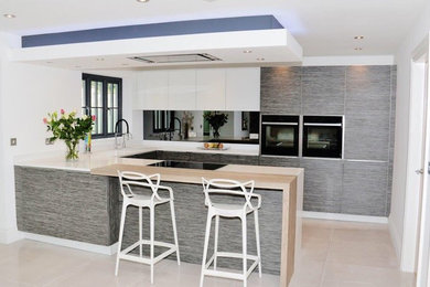 This is an example of a medium sized contemporary u-shaped kitchen/diner in Other with an integrated sink, flat-panel cabinets, grey cabinets, quartz worktops, grey splashback, glass tiled splashback, black appliances, ceramic flooring and a breakfast bar.