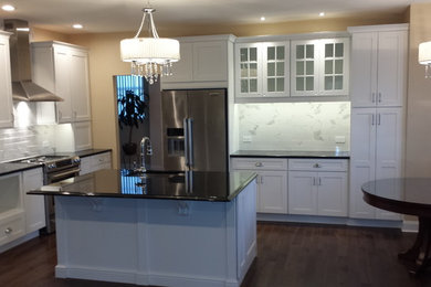Large transitional l-shaped dark wood floor kitchen photo in Philadelphia with an undermount sink, recessed-panel cabinets, white cabinets, granite countertops, white backsplash, ceramic backsplash, stainless steel appliances and an island
