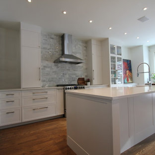 Mid-sized shabby-chic style u-shaped eat-in kitchen in Calgary with a farmhouse sink, flat-panel cabinets, white cabinets, quartzite benchtops, multi-coloured splashback, marble splashback, stainless steel appliances, dark hardwood floors, with island, brown floor and white benchtop.