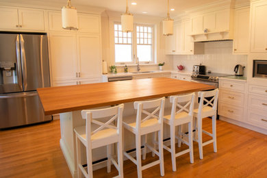 Example of a large transitional l-shaped medium tone wood floor and brown floor eat-in kitchen design in Ottawa with a double-bowl sink, shaker cabinets, white cabinets, wood countertops, white backsplash, stainless steel appliances, an island and brown countertops