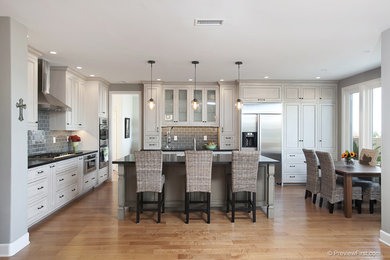 Eat-in kitchen - large traditional l-shaped light wood floor eat-in kitchen idea in San Diego with raised-panel cabinets, white cabinets, an island, a farmhouse sink, soapstone countertops, gray backsplash, subway tile backsplash and stainless steel appliances