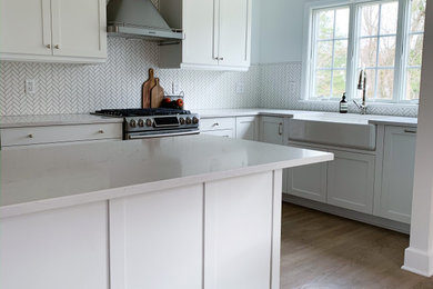 Enclosed kitchen - mid-sized traditional l-shaped vinyl floor and brown floor enclosed kitchen idea in New York with a farmhouse sink, shaker cabinets, white cabinets, white backsplash, ceramic backsplash, stainless steel appliances, a peninsula and white countertops