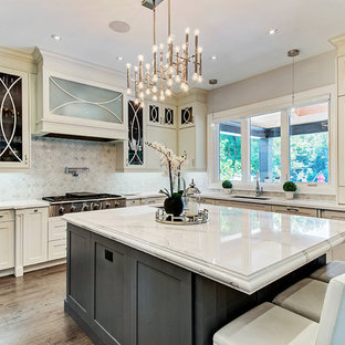 Photo of a transitional l-shaped kitchen in Toronto with an undermount sink, glass-front cabinets, beige cabinets, grey splashback, stainless steel appliances, dark hardwood floors, with island, brown floor and white benchtop.