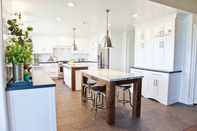 Example of a mid-sized transitional u-shaped ceramic tile enclosed kitchen design in Salt Lake City with a farmhouse sink, shaker cabinets, white cabinets, granite countertops, white backsplash, subway tile backsplash, stainless steel appliances and two islands