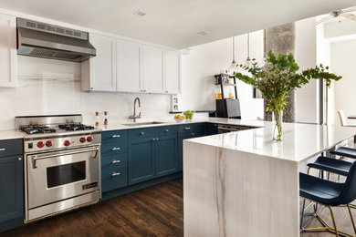 Example of a mid-sized eclectic u-shaped medium tone wood floor and brown floor open concept kitchen design in New York with an undermount sink, shaker cabinets, blue cabinets, marble countertops, white backsplash, marble backsplash, stainless steel appliances, a peninsula and white countertops