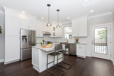 Example of a large transitional l-shaped dark wood floor and brown floor eat-in kitchen design in New York with a farmhouse sink, shaker cabinets, white cabinets, quartzite countertops, white backsplash, subway tile backsplash, stainless steel appliances and an island