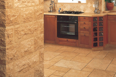 Example of a mid-sized trendy l-shaped limestone floor eat-in kitchen design in New York with an undermount sink, glass-front cabinets, medium tone wood cabinets, quartzite countertops, beige backsplash, stone tile backsplash, black appliances and an island