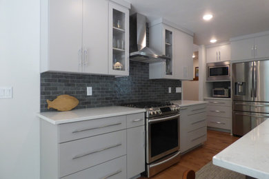 Mid-sized trendy l-shaped medium tone wood floor and brown floor eat-in kitchen photo in Other with an undermount sink, flat-panel cabinets, dark wood cabinets, granite countertops, gray backsplash, subway tile backsplash, stainless steel appliances, an island and white countertops