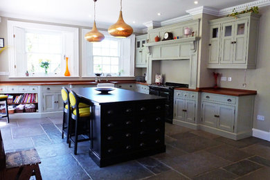Offene Landhaus Küche in L-Form mit Kassettenfronten, Kücheninsel, grauen Schränken und schwarzen Elektrogeräten in Sonstige